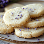 Delicate lavender-infused shortbread cookies topped with edible lavender, served on a ceramic plate.