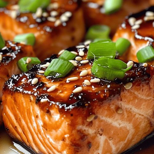 "Glazed salmon bites garnished with green onions and sesame seeds, served on a white plate."